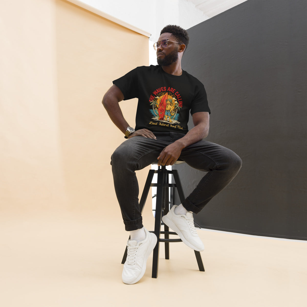 Model wearing a black T-shirt with a vibrant graphic of a dog holding a surfboard, surrounded by tropical scenery and the phrase 'The Waves Are Calling' SKU: 5484311_12634