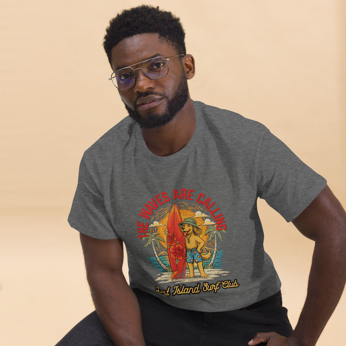 Man wearing dark gray T-shirt with colorful tropical surfing scene, posing against beige background, casual fashion style